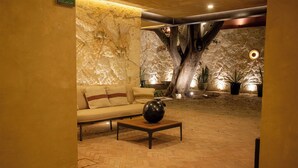 Ein Zimmer mit einer Couch, einem Couchtisch, einer großen Vase und einer Wand mit Baum- und Pflanzenmotiven.