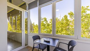A room with a table and chairs, large windows, and a view of trees and a building outside. - Central Tirana 1BR Apartment Near Main Square by PikHost (Tiranë)