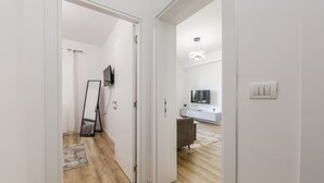 A hallway with a wooden floor, a white door, a mirror, a TV on the wall, and a modern light fixture. - Central Tirana 1BR Apartment Near Main Square by PikHost (Tiranë)