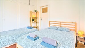 Een kamer met twee bedden, een houten hoofdbord, een tafeltje met een lamp en een plank met planten.