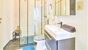 Een badkamer met een douchecabine van glas, een wit toilet, een wastafel met een handdoek en een spiegel.
