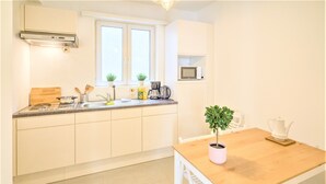 Een keuken met witte kasten, een houten aanrecht, een raam, een magnetron en een eettafel met stoelen.