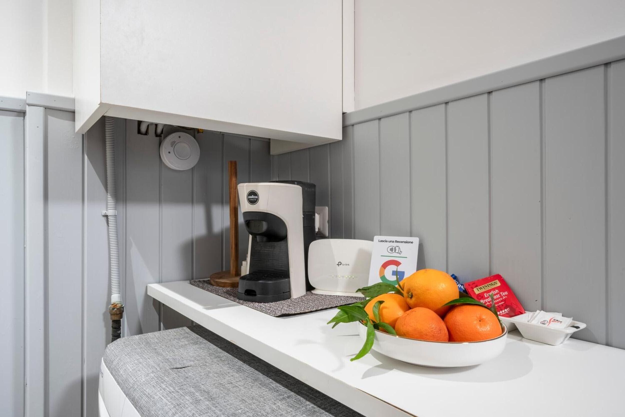 Una kitchenette equipada con cafetera, un refrigerador pequeño y un tazón de naranjas.