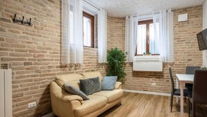 A furnished room with a brick wall, a beige sofa, a dining table, and a potted plant. - Charming Apartment Maison all'arco (Corridonia)