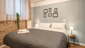 A bedroom with a bed, bedside tables, a lamp, a window with sheer curtains, and a brick wall. - Charming Apartment Maison all'arco (Corridonia)