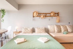 A bedroom with a bed, a sofa, a bedside table with a lamp, and a wall-mounted hat rack.