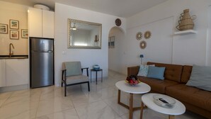 Una sala moderna con un sofá, dos mesas pequeñas, una silla y una cocina con un refrigerador.
