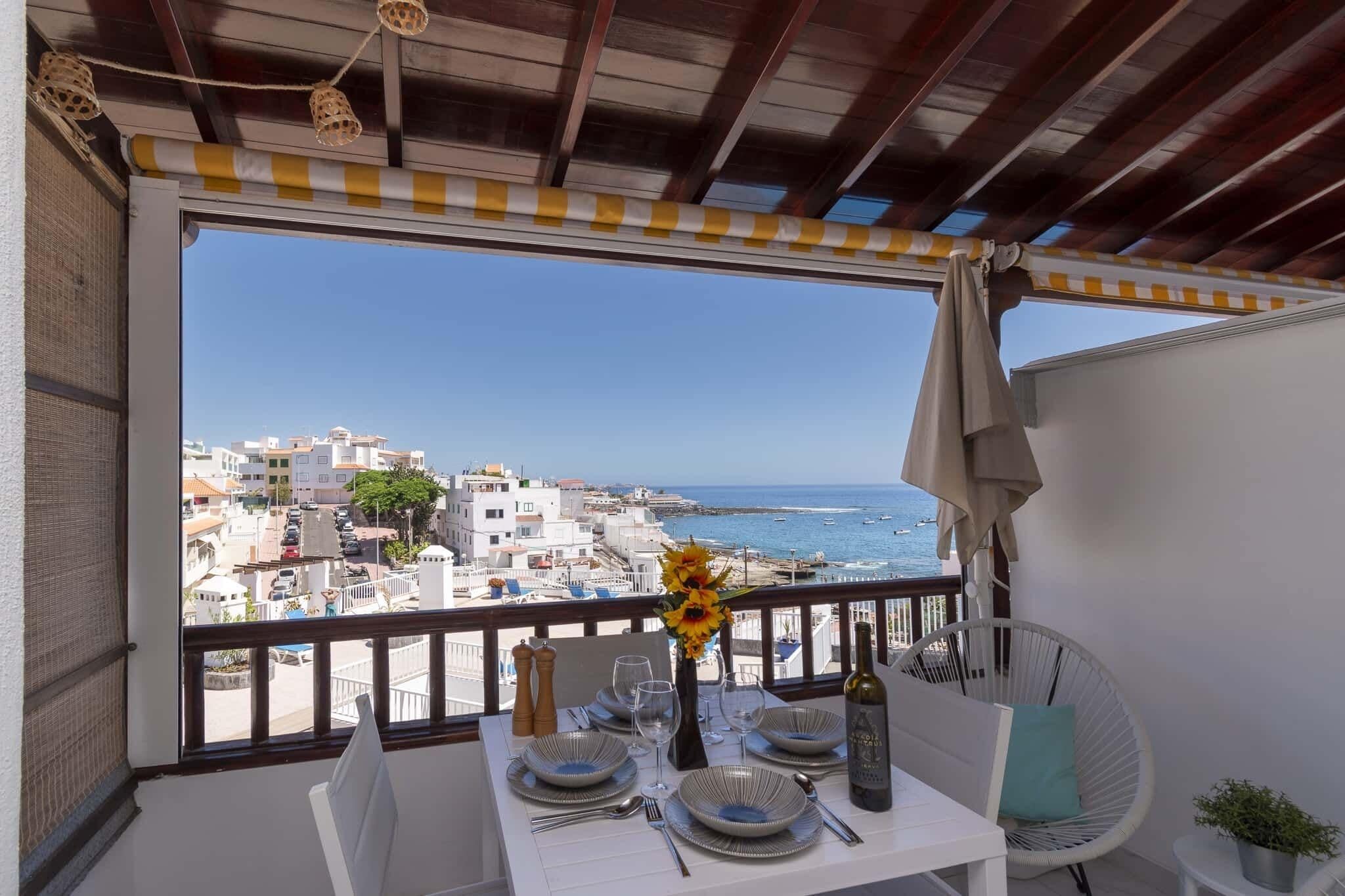 A balcony with a table set for dining, overlooking a coastal cityscape with buildings and the sea.