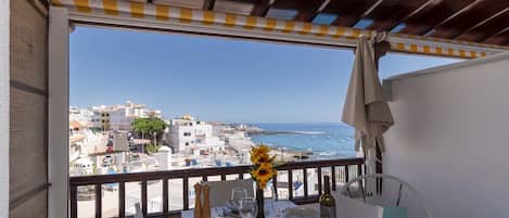 A balcony with a table set for dining, overlooking a coastal cityscape with buildings and the sea.