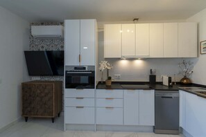 Eine moderne Küche mit weißen Schränken, einem Einbauofen, einem Geschirrspüler und einem flachbildfernseher an der Wand.