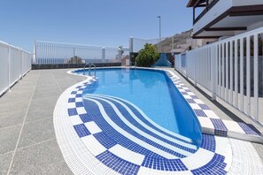 Una piscina amb una terrassa enrajolada i una tanca blanca al voltant.