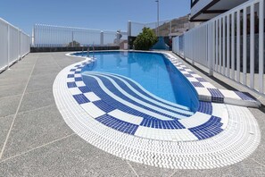 Ein Schwimmbecken mit einer gefliesten Terrasse und einem weißen Zaun darum.