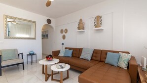 Una sala de estar moderna con un sofá de cuero marrón, dos mesitas redondas blancas, una silla y decoración en la pared.