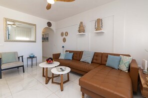 Ein modernes Wohnzimmer mit einer braunen Ledersofa, zwei weißen runden Tischen, einem Sessel und Wanddekoration.