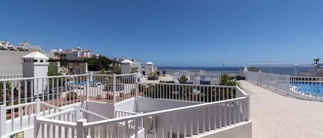 A rooftop terrace with a pool, white railings, and a clear view of the sea.