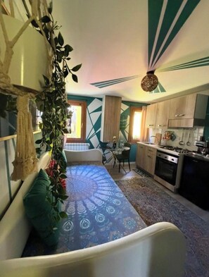 Een knus woongedeelte met een bank, een eettafel, een keukenhoek en een hangplant.