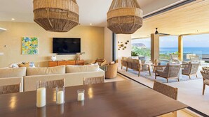 A modern living room with a large sofa, a dining table with candles, wicker pendant lights, and a view of the ocean. - Costa Azul at Kupuri Beach Residences (Desarrollo Punta Mita)