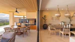 A modern kitchen with a built-in grill, a dining area with a round table, and a view of the outdoors. - Costa Azul at Kupuri Beach Residences (Desarrollo Punta Mita)