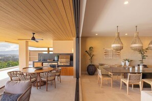 Eine moderne Küche mit integriertem Grill, einem Essbereich mit rundem Tisch und Blick ins Freie.