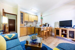 Sala de estar com sofá, mesa de centro, televisão e área de cozinha com armários e micro-ondas.