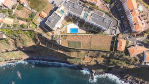 Vista aerea di una proprietà costiera con piscina, giardini a terrazze e un litorale roccioso.