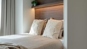 Una cama con cabecera de madera, una ventana con cortinas y una pequeña planta en la cabecera.