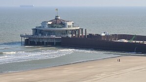 Un edificio costero con una estructura en forma de cúpula, un muelle que se adentra en el agua y una playa arenosa en primer plano.