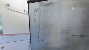 Un baño moderno con ducha envuelta en vidrio, inodoro blanco y lavamanos con dispensador de jabón azul.