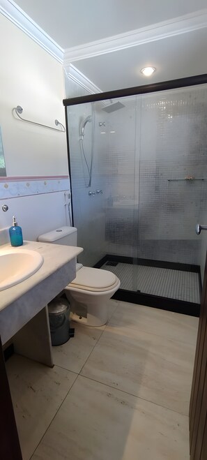 Ein modernes Badezimmer mit einer Duschkabine, einer weißen Toilette und einem Waschbecken mit blauem Seifenspender.