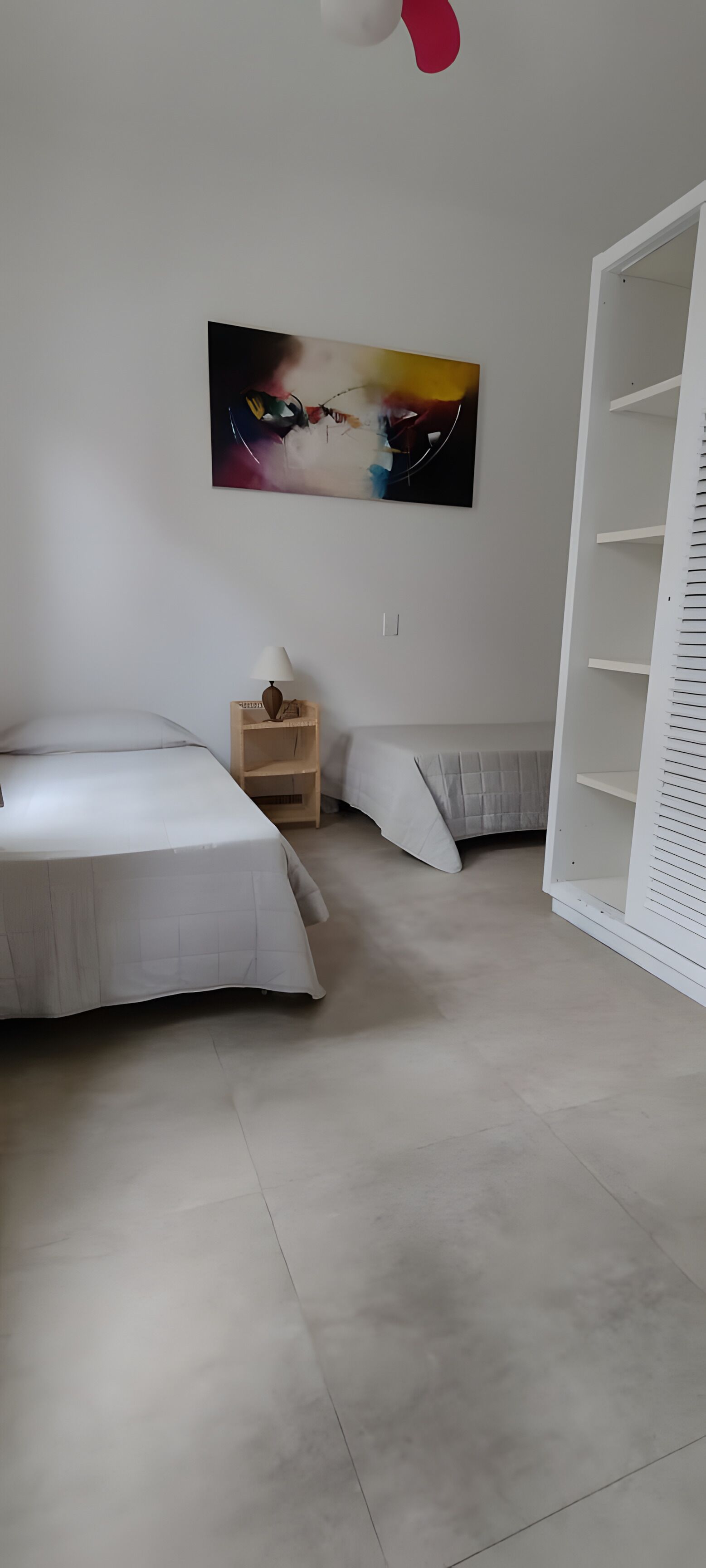 A bedroom with two beds, a wooden nightstand, a white wardrobe, and a painting on the wall.