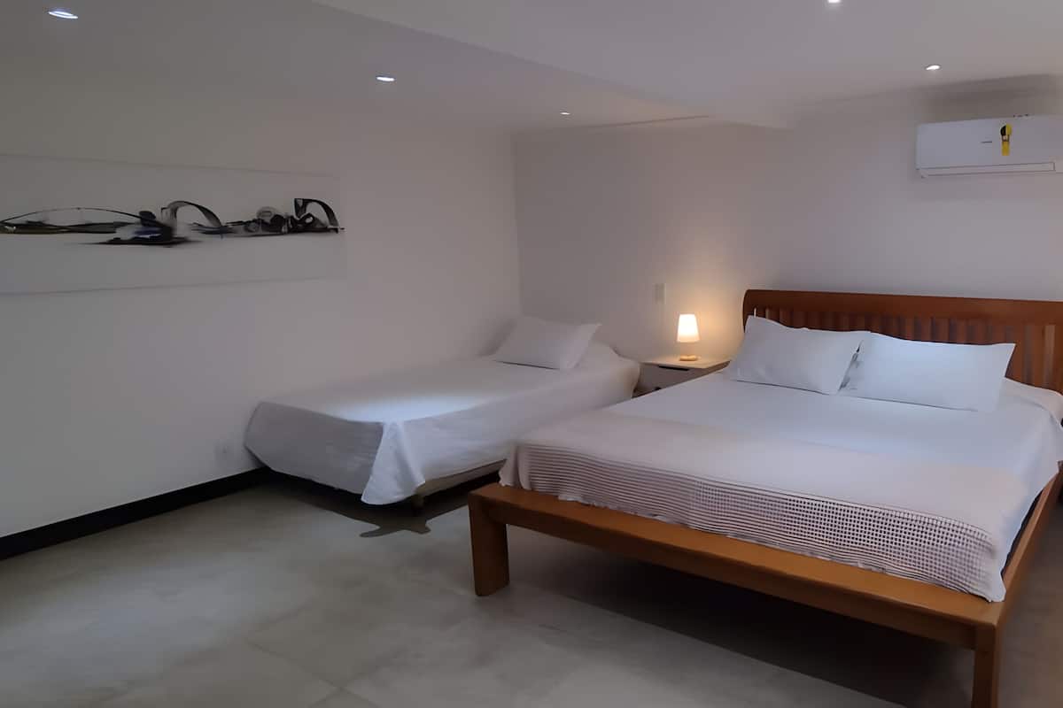 A hotel room with a large bed, two bedside tables, a wall-mounted air conditioner, and a window.