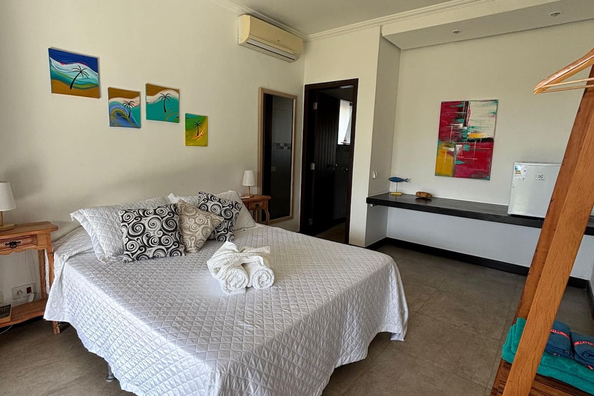 A bedroom with a bed, pillows, a ceiling fan, artwork on the wall, and a door leading to another room.