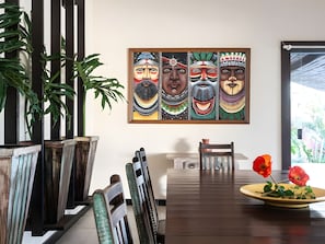 Un coin repas avec une table en bois, des chaises, un tableau accroché au mur et des plantes en pot.