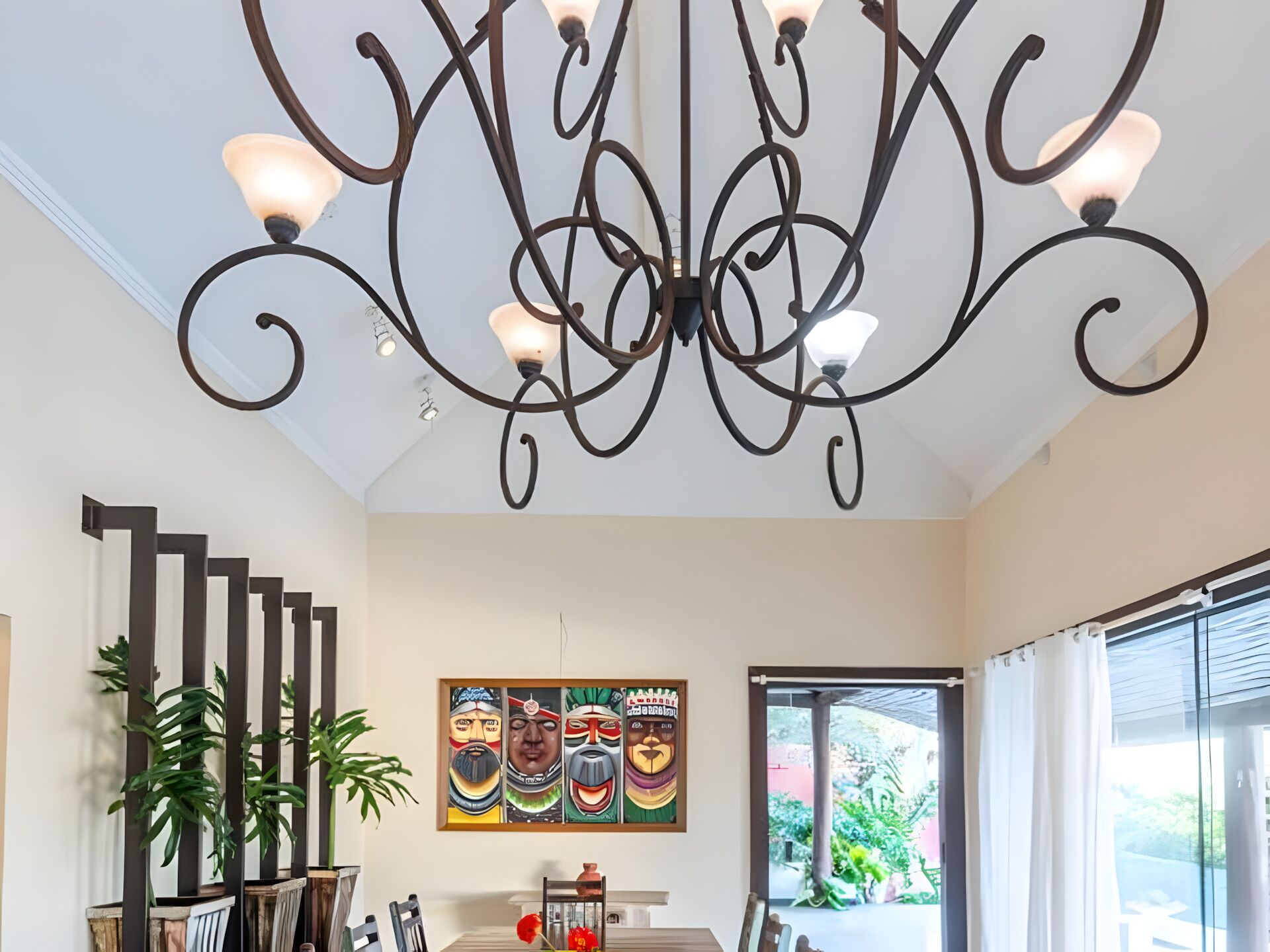 Un comedor con candelabro, obras de arte, plantas en macetas y vistas a través de un amplio ventanal.