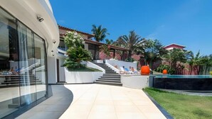 Ein modernes Gebäude mit einer geschwungenen Fassade, einer Treppe zu einem Poolbereich und einem strahlend blauen Himmel.