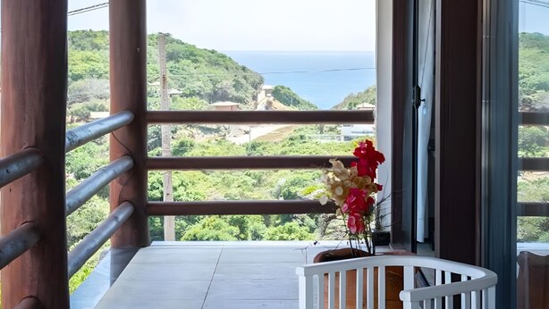Un balcón con vistas al mar, barandal blanco y una maceta con flores.