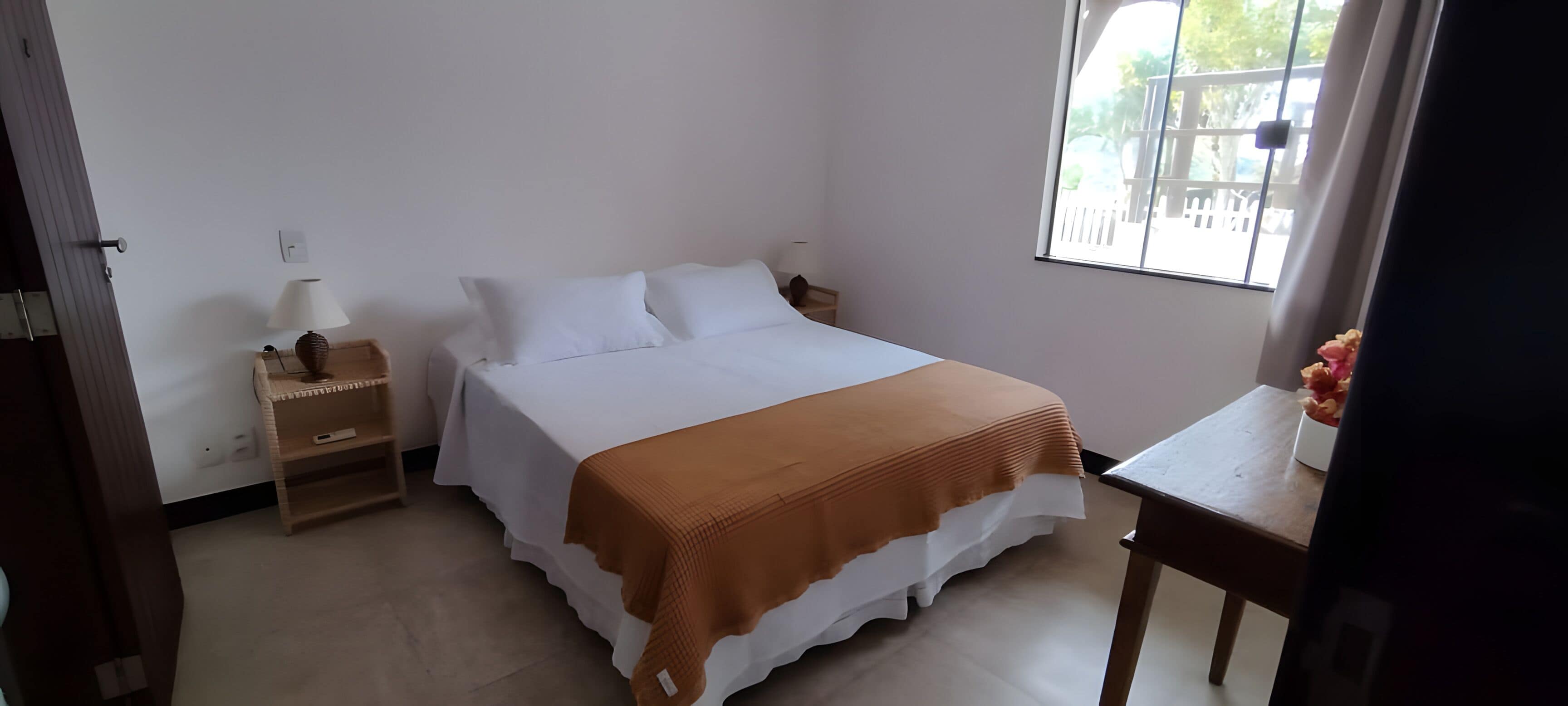 A bedroom with a bed, bedside tables, a lamp, a window, and a view of the outside.