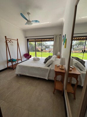 A bedroom with a bed, a wooden swing, a chair, a bedside table, and a view of the outdoors. -  Pousada Ganesha Búzios (Buzios)