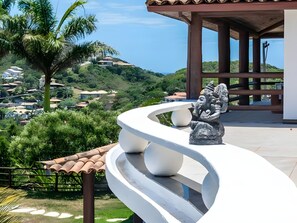 A curved white balcony with a stone sculpture, overlooking a lush green landscape with houses and a clear sky. -  Pousada Ganesha Búzios (Buzios)