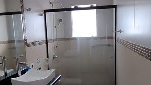Un baño moderno con cabina de ducha de vidrio, un lavabo blanco y un inodoro.