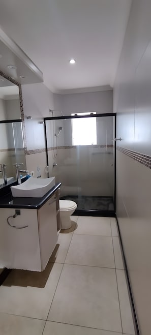 Ein modernes Badezimmer mit Duschkabine aus Glas, einem weißen Waschbecken und einer Toilette.