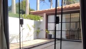 Una habitación con un gran ventanal corredero que da a un espacio exterior cubierto con palmeras y una pared blanca.