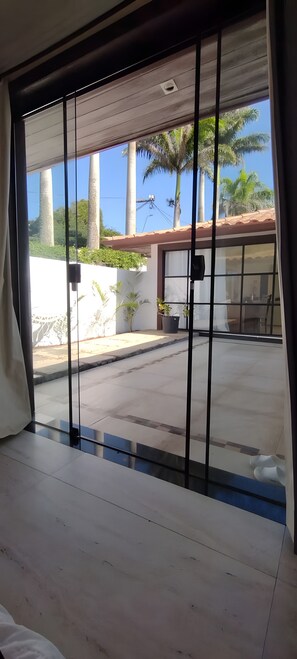Ein Zimmer mit einer großen Schiebeglasdoor, die zu einem überdachten Außenbereich mit Palmen und einer weißen Mauer führt.