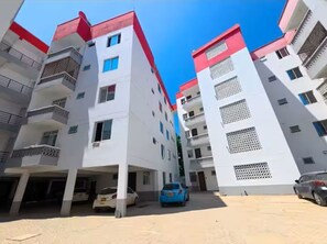 A multi-story residential building with balconies, a parking area, and a clear blue sky. - Stylish Mtwapa Studio with Rooftop Pool View (Mtwapa)