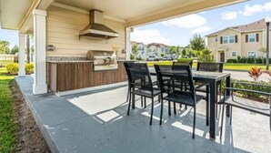 Un patio al aire libre con una parrilla y zona de comedor, rodeado por un corredor cubierto.