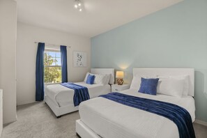 A bedroom with two beds, a window with curtains, a bedside table with a lamp, and a wall-mounted artwork. - Modern Townhome 3 BD/ 2 BA/ West Lucaya (8980 SP) (Kissimmee)