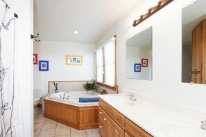 A bathroom with a bathtub, a sink, wooden cabinets, and a large mirror. - Springer's Retreat - Ocracoke Island (Ocracoke)