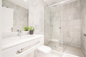 Ein modernes Badezimmer mit einer gläsernen Duschkabine, einer weißen Toilette und einem Waschtisch mit Spiegel und Waschbecken.