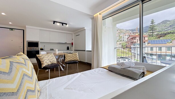 Une chambre d’hôtel moderne avec balcon, un coin cuisine et un lit donnant sur une vue agréable.