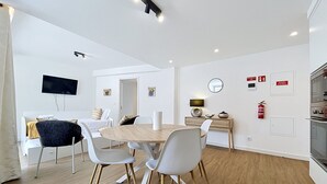 Une cuisine moderne dotée d’un four encastré, un coin repas avec une table ronde et des chaises blanches, et un téléviseur fixé au mur.
